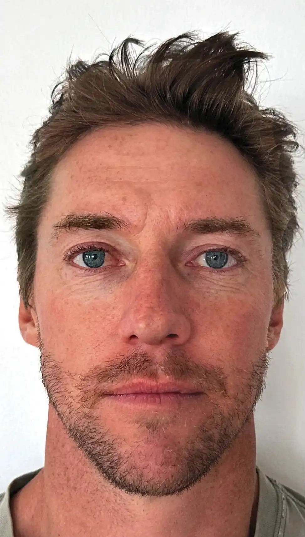 Close-up of a person with short hair and a neutral expression on a white background