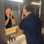 Man applying skincare product in front of a bathroom mirror.